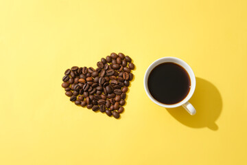 Coffee beans arranged in a heart shape and a cup of black coffee on a yellow background. Applying a coffee mask helps fade freckles and repel tiny wrinkles related to aging.