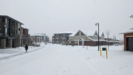 walking down a road in a residential area during a winter storm in Ottawa, Ontario. Road is covered by snow. Pedestrian can be seen on the left. 