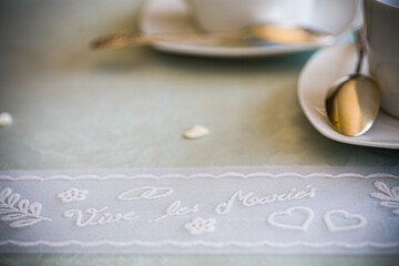 The photograph offers a tender glimpse into a wedding celebration, focusing on the beautifully set table. A gleaming spoon and a partially visible cup and saucer blur softly into the background