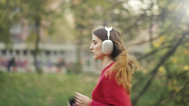 Waist Up Side Shot Following Young White Woman Jogging With Headphones. Concept of Aspiring Athlete, Olympic Games, Paris 2024