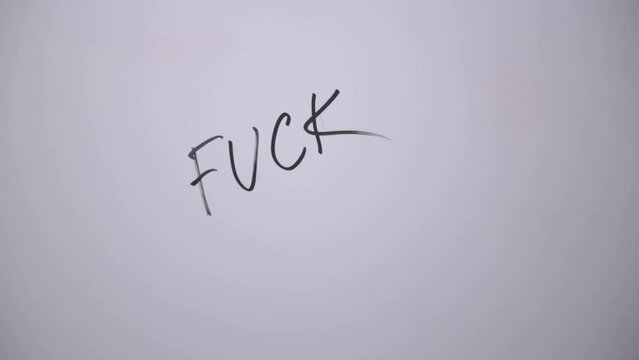 FUCK. A woman's hand writes the word FUCK with a black marker on a white board. Writes a word with anger