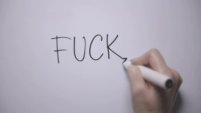 FUCK. A woman's hand writes the word FUCK with a black marker on a white board. Writes a word with anger
