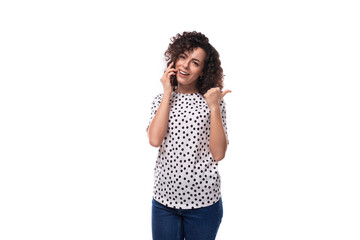 a slender young stylish woman with a curly haircut dressed in a blouse with polka dots speaks on...