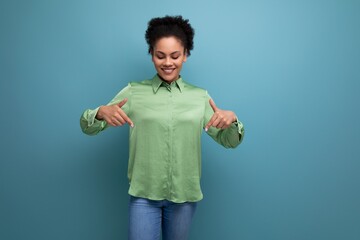 young cheerful latin business lady in green blouse showing hands down on studio background with...