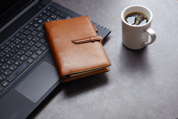 コーヒーを飲みながら、ノートパソコンとシステム手帳でデスクワークをしているイメージ
