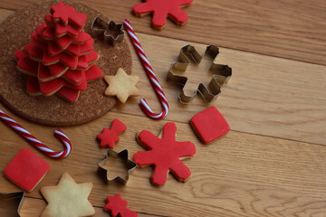 Christmas tree made of star shaped shortcrust cookies with red sugar glaze with cookie cutters candy canes and other cookies on wooden table. Christmas background