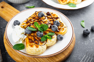 Homemade waffles with blueberries, chocolate sauce and cream cheese in a plate and a grey background close up
