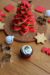 Christmas tree made of star shaped shortcrust cookies with red sugar glaze with cookie cutters, glass ornaments and other cookies on wooden table. Christmas background