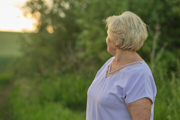The golden light of the evening sun highlights the face of a smiling elderly woman, surrounded by the tranquility of nature.