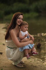 A woman cradles her child at the water's edge, ducks milling around a portrayal of maternal instinct and wildlife coexistence.