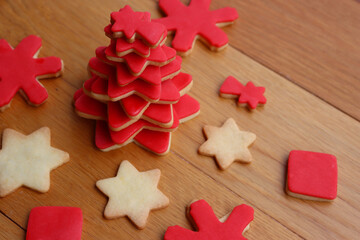 Christmas tree made of star shaped shortcrust cookies with red sugar glaze and other cookies on wooden table. Christmas background