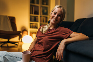 Beautiful woman smiling at the camera and sitting on the floor at home.