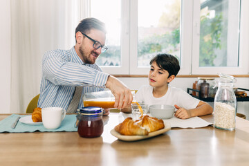 Father is pouring juice for his son during breakfast.