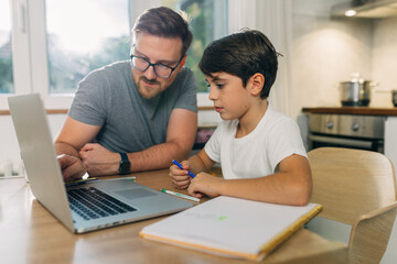 A Caucasian man is helping his son study.