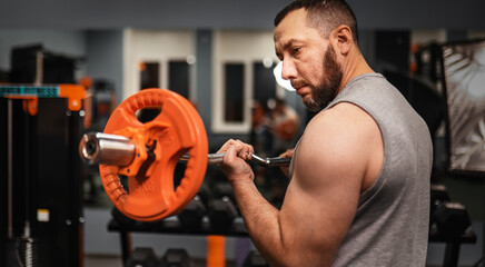 An ordinary man pumping muscles with a barbell in the gym. The concept of weight training for all...