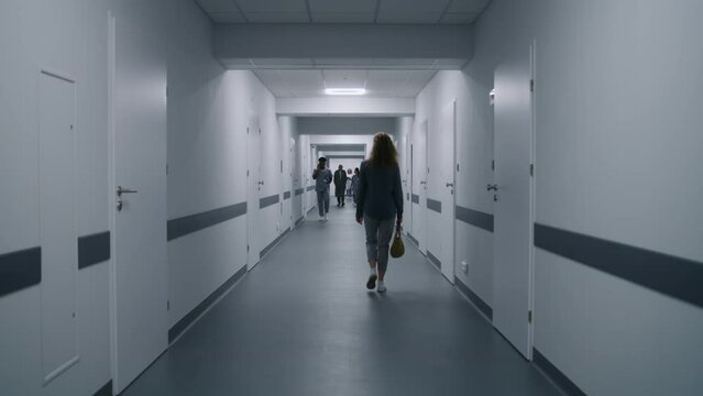 Woman goes hospital corridor and asks doctor way to cabinet. Nurse and elderly patient walk clinic hallway and discuss tests results. Multi ethnic medical staff in clinic. Static shot. Back view.