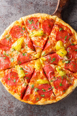 Italian salami pizza with peperoncini peppers, mozzarella and herbs close-up on a wooden board on the table. Vertical top view from above