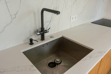 Black kitchen sink and Tap water in the kitchen. The interior of the kitchen room of the apartment. Built-In Appliances. Kitchen Appliance. Domestic Appliances.