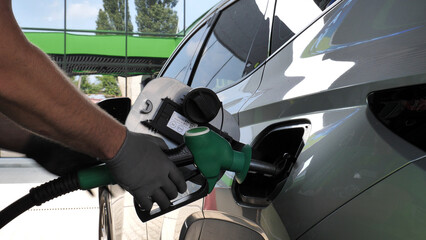 Assistant at petrol station hands in gloves inserting a fuel pistol into the gas tank of a car
