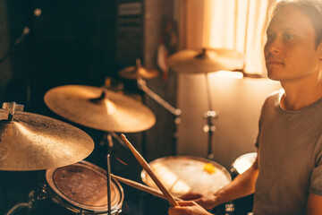 Drummer plays drums in music studio at band rehearsal. Musician with instrument in beautiful sunset light from window.