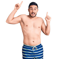Fototapeta premium Young handsome man wearing swimwear smiling amazed and surprised and pointing up with fingers and raised arms.