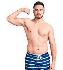 Young handsome man wearing swimwear strong person showing arm muscle, confident and proud of power