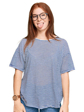 Young read head woman wearing casual clothes and glasses sticking tongue out happy with funny expression. emotion concept.