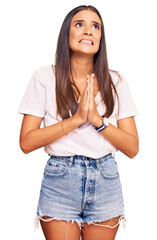 Young hispanic woman wearing casual white tshirt begging and praying with hands together with hope expression on face very emotional and worried. begging.