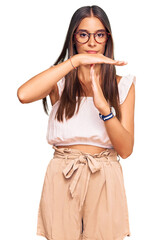 Young hispanic woman wearing casual clothes and glasses doing time out gesture with hands,...