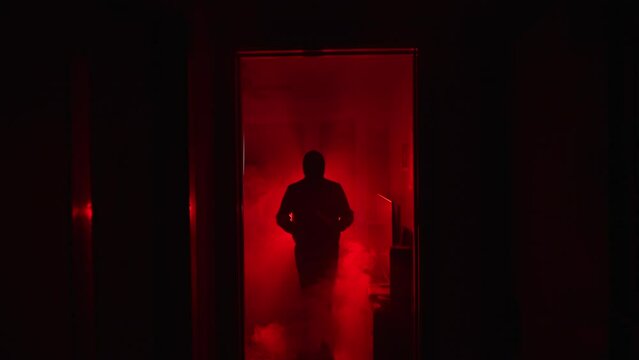 Slow motion zoom of evil shadowy figure holding knife in glowing red fog