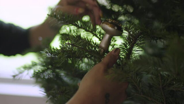 Woman clips festive holiday ornament to a Christmas tree during the holiday season. slow motion, close up
