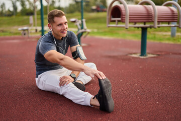 Young male athlete listening to music while stretching outdoors