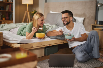 Happy couple having breakfast in bed and using laptop