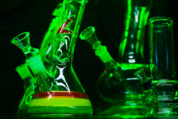 Glass flasks for smoking marijuana herb under green lighting. Herb smoking device.