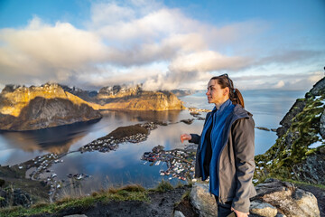 young woman taking a look from the height of Reinebringen on fisherman reine village on lofoten...