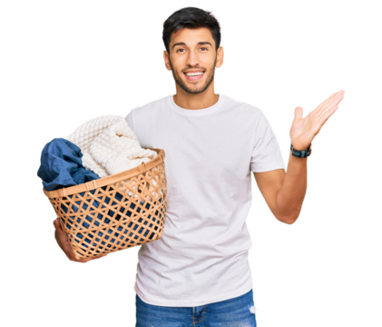 Young handsome man holding laundry basket celebrating victory with happy smile and winner expression with raised hands