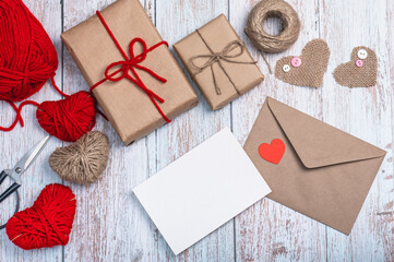 A craft envelope, a blank form, a heart shape made of burlap, red thread and twine and two craft gift boxes on a wooden background. DIY gifts.