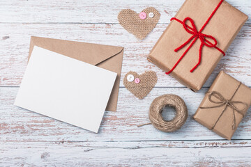 Craft envelope, blank form, burlap heart shapes and two craft gift boxes on a wooden background....