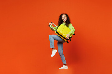 Full body traveler woman in casual clothes hold suitcase bag pov play guitar isolated on plain orange background Tourist travel abroad in free spare time rest getaway Air flight trip journey concept - obrazy, fototapety, plakaty