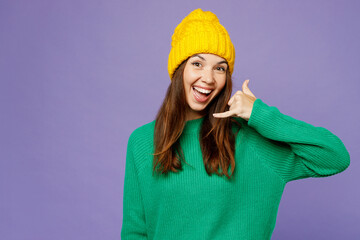 Naklejka premium Young excited happy woman wear green sweater yellow hat casual clothes doing phone gesture like says call me back isolated on plain pastel light purple background studio portrait. Lifestyle concept.