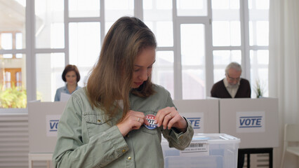 Portrait of a young responsible woman attaching a vote button to her chest during elections