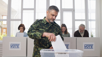 A military man, a soldier, putting a voting ballot into the box at the polling place during...