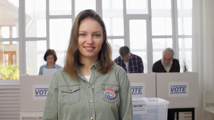 A proud responsible woman standing at the voting place with an attached vote button on her chest