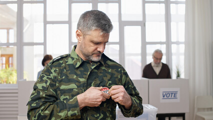 Middle-aged soldier in military uniform attaching a vote pin at the polling station