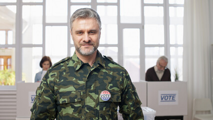 Portrait of a soldier with a vote pin at the polling place, exercising his voting right and civic...
