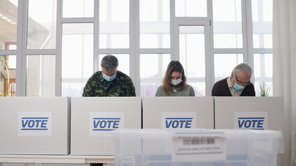 People in protective face masks voting at the polling place during elections amid the pandemic