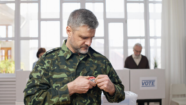 Middle-aged soldier in military uniform attaching a vote pin at the polling station