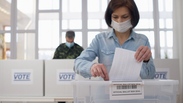 A woman in a protective face mask throwing a voting ballot into a special election box