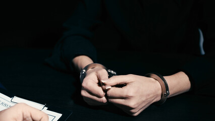 A close-up of female hands in handcuffs on a table near papers with information after interrogation