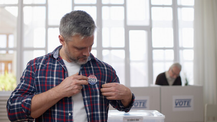A Caucasian middle-aged man is attaching a vote button to his chest at the polling station